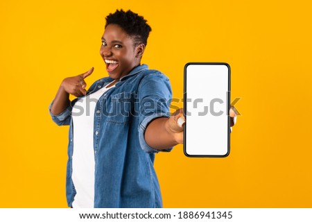 Mobile Application Ad. Excited African Woman Showing Phone Empty Screen Recommending App Standing Over Yellow Studio Background, Smiling To Camera. Cellphone Display Mockup, Check This Apps