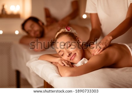 Couple Relaxing Receiving Back Massage Lying Closing Eyes At Romantic Luxury Spa With Burning Candles And Flowers. Wellness And Body Relaxation Therapy. Selective Focus, Low Light