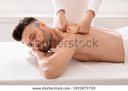 Middle aged bearded man attending modern male spa, laying on massage table, getting healing body procedure, enjoying his day at spa. Masseuse pressing on man back, using acupressure technique