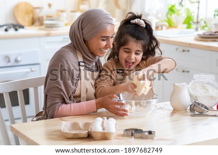 Cheerful Muslim Mom In Hijab And Her Little Daughter Having Fun At Home, Baking Pastry In Kitchen Together, Kneading Dough While Preparing Cookies, Enjoying Cooking Homemade Food. Closeup Shot
