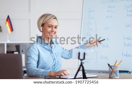 Online languages school. Millennial female tutor giving German lesson on internet, using smartphone, pointing at blackboard, explaining grammar to remote students. Education during covid-19 epidemic ストックフォト © 