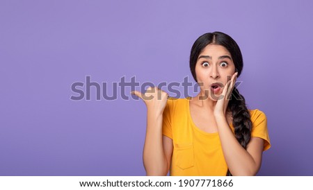 Omg, Cool Offer. Surprised young indian lady pointing at free space isolated over purple studio background. Excited shocked woman showing copy space and place for advert or promotional text, banner 商業照片 © 