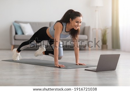 Cheerful active woman doing fitness at home, using laptop, watching online lessons. Positive well-fit lady in sportswear exercising during covid-19 pandemic, watching fitness videos on Internet
