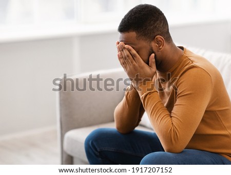 Male Depression. Desperate Depressed African Man Covering Face Crying Having Problems Sitting On Couch At Home. Emotional Stress And Unhappiness Concept. Despair, Grief And Negative Emotions