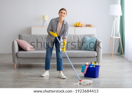 Pretty young lady wiping floor with mop, doing house cleanup, free space. Positive housewife tidying her apartment, doing household chores. Professional sanitary service concept