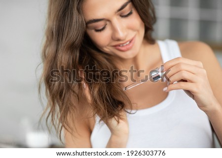 Split Ends Haircare And Repair Treatment. Woman Applying Oil To Prevent Hair Breakage Holding Dropper Standing In Modern Bathroom At Home. Remedy And Care For Beauty Of Damaged Hair. Selective Focus