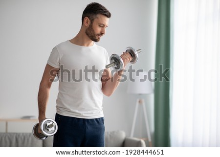 Closeup of handsome middle-aged man doing dumbbell workout at home, working on arms strength, looking at his biceps, copy space. Athletic man lifting dumbells up over living room interior Photo stock © 