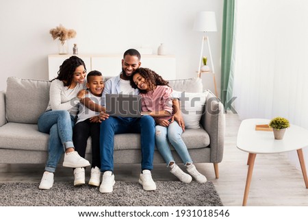 Family Weekend. Portrair of cheerful African American parents and their little children using laptop at home together, watching movie or browsing internet, sitting on the couch in living room