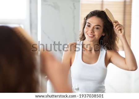 Cheerful Female Combing And Brushing Her Wavy Hair In Bathroom