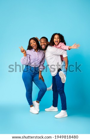 Spending Time With Family Is Fun. Full body length of excited African American man, woman and girl laughing and posing isolated over yellow studio wall. Cheerful father carrying his daughter on back