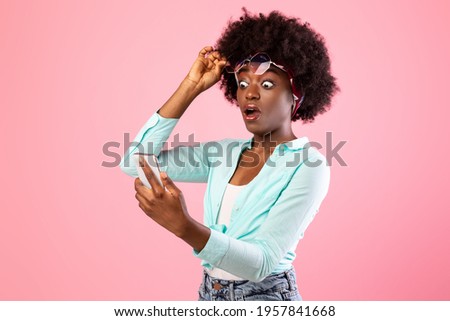 Wow Application. Extremely Shocked African Woman Looking At Smartphone Reading Message With Exciting Shocking News Holding Eyeglasses Posing Over Pink Studio Background. New Mobile App For Phone