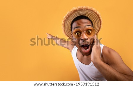 Summer sale. Shocked black guy in straw hat pointing at empty space on yelow studio background. Surprised African American man advertising your summertime product or service 商業照片 © 