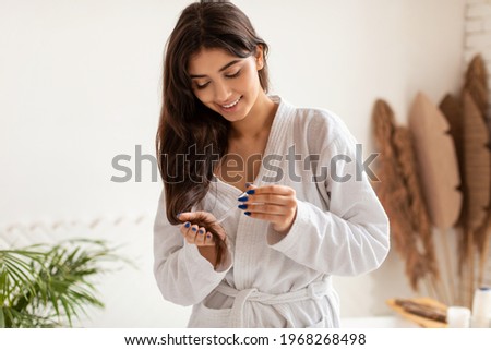 Haircare, Split Ends Treatment. Woman Applying Serum Or Essential Oil Caring For Damaged Dry Hair Posing Standing In Modern Bathroom At Home. Beauty Routine Concept