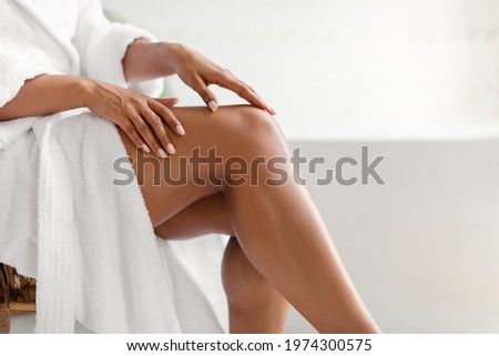 Side View Of Unrecognizable Black Lady Touching Perfect Smooth Legs After Depilation Posing Sitting On Chair In Bathroom At Home. Cropped Shot Of Female Legs. Hair Removal And Body Care Imagine de stoc © 
