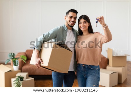 House Ownership. Young Couple Showing Keys And Holding Cardboard Box, Cheerful Guy And Lady Hugging After Moving In New Apartment Standing In Living Room. Insurance, Real Estate, Mortgage Concept Foto stock © 
