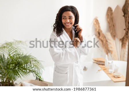 Haircare Routine. Happy African American Lady Touching Wet Hair After Shower Posing Standing In Modern Bathroom At Home. Cosmetics For Hair And Beauty Care Concept