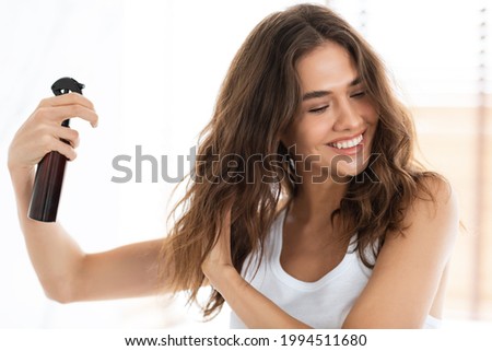 Hairspray Advertisement. Happy Woman Applying Spray On Wavy Hair For Detangling Caring For Herself Standing In Modern Bathroom Indoors. Hairstyling Product For Split Ends