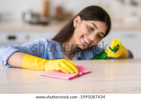 Cleanliness Concept. Closeup of smiling young woman wearing protecitve yellow rubber gloves cleaning table, holding spray bottle and using microfiber cloth, wiping dust, selective focus on hand Imagine de stoc © 