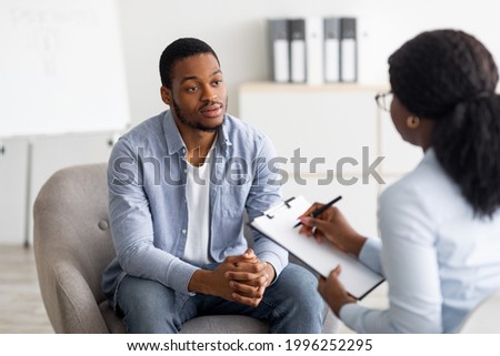 Unhappy young black man having session with professional psychologist at mental health clinic. Psychotherapist taking notes during conversation with depressed male patient Stock foto © 