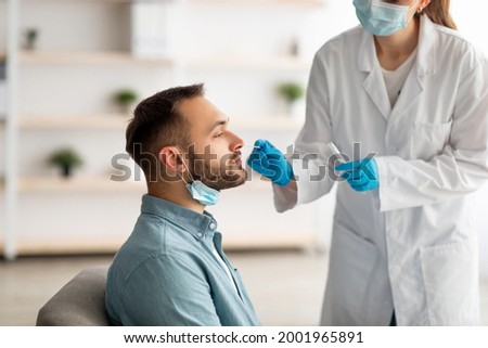 Covid diagnostic procedure. Doctor making nasal PCR test for young Caucasian man, using sterile swab stick at home. Millennial guy undergoing coronavirus analysis, checking health