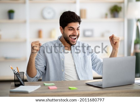 Promotion news. Excited arab man looking at laptop and celebrating his success, sitting at home office workplace, raising fists and exclaiming with joy, emotionally reacting to email Foto stock © 