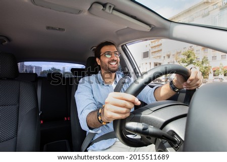 Joyful indian man driving car, shot from dashboard, going on trip during summer vacation, copy space. Happy middle-eastern guy in casual outfit and glasses driving his brand new nice car Foto stock © 