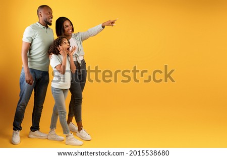 Wow offer. Full body length portrait of excited black family looking and pointing aside at copy space on yellow background, demonstrating free place for your advert, panorama, banner