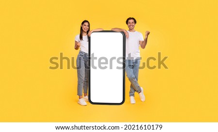 Yes. Excited Couple Leaning On Big Smartphone With Empty White Screen Shaking Clenched Fists, Cheerful Guy And Lady Celebrating Win, Standing On Yellow Background, Mock Up Collage, Full Body Length