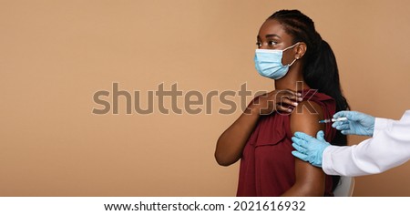 Side view of young black woman patient wearing protective face mask getting vaccination against coronavirus while COVID-19 pandemic, nurse making injection in shoulder, panorama with copy space