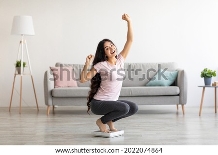 Overjoyed Indian woman sitting on scales, gesturing YES, excited over result of her weight loss diet at home. Millennial Asian lady achieving her slimming goal, copy space Foto stock © 