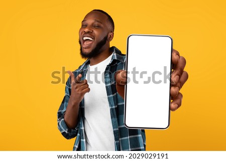 Recommendation. Portrait of excited black guy holding big smartphone with white blank screen in hand, showing close to camera and pointing at device. Gadget with empty free space for mock up, banner 商業照片 © 