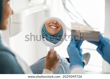 Beautiful Muslim Woman In Hijab Looking At Mirror In Dentists Office, Islamic Female Patient Enjoying Her Beautiful Smile And Teeth After Dental Treatment In Stomatologic Clinic, Selective Focus Сток-фото © 