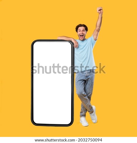 Yes, Big Luck. Excited Guy Leaning On Smart Phone With Empty White Screen Shaking Clenched Fist Raising Hand Up, Cheerful Man Celebrating Win, Looking At Camera, Standing At Studio, Mock Up Collage