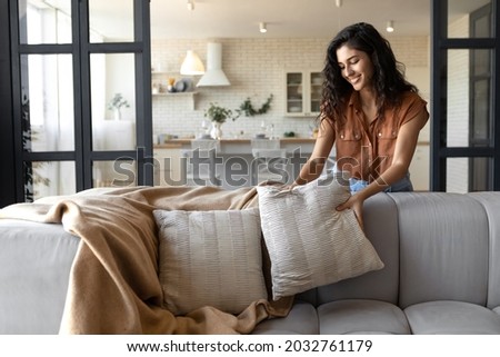 Lovely young woman putting soft pillows and plaid on comfy sofa, making her home cozy and warm, copy space. Millennial lady decorating her couch with cushions and blanket for autumn or winter Foto stock © 