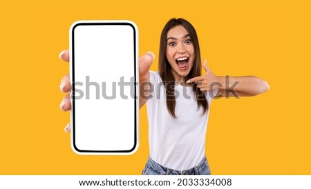 Great Mobile Offer. Excited Lady Pointing Finger At Smartphone In Her Hand, Emotionally Reacting To New App, Overjoyed Millennial Woman Standing Isolated Over Orange Studio Background, Panorama ストックフォト © 