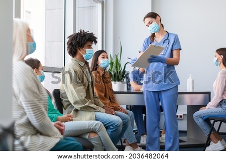 Coronavirus Vaccination Campaign Concept. Female doctor or nurse in uniform holding clipboard while talking to patients sitting and waiting in line at medical clinic, showing consent form to sign Imagine de stoc © 