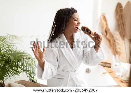 Black Young Woman Enjoying Haircare Singing With Hairbrush Having Fun While Brusing Hair After Shower Standing In Bathroom At Home. Haircare Cosmetics Advert. Female Beauty Routine