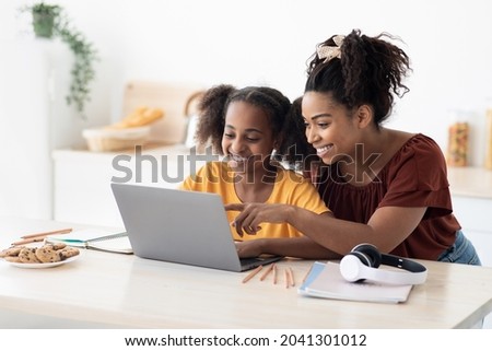 Creative black mother and daughter working on school project, using modern laptop, taking notes, cheerful afro-american woman helping her teen kid with homework, kitchen table, copy space 商業照片 © 