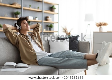 Rest And Relax Concept. Calm asian man sitting on couch, listening to music, audio book, podcast, enjoying meditation for sleep and peaceful mind in wireless headphones, leaning back, copy space Photo stock © 