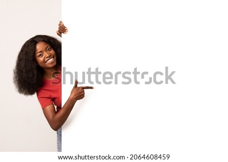 Check This. Smiling African American Lady Pointing Aside At Copy Space On Blank White Advertisement Board With Finger, Positive Black Woman Showing Free Place For Your Design On Empty Billboard 商業照片 © 