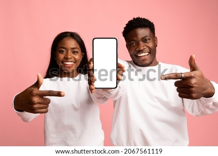 Cheerful african american young people beautiful mana nd woman in white showing modern smartphone with blank screen, mockup, pointing at advertising, posing on pink studio background Imagine de stoc © 