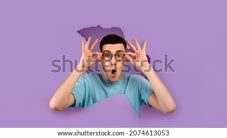 Wow, Unbelievable Offer. Portrait of shocked man in glasses with amazed expression looking through torn hole in violet paper. Panorama, banner, free copy empty space for advertising, purple background Foto d'archivio © 