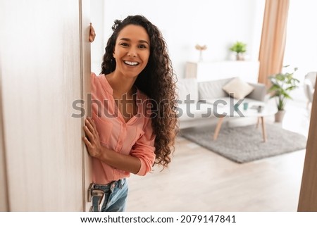 Welcome. Portrait of cheerful woman standing in doorway of modern apartment, greeting visitor and inviting guest to enter her home, happy smiling young lady holding door looking out flat Foto stock © 