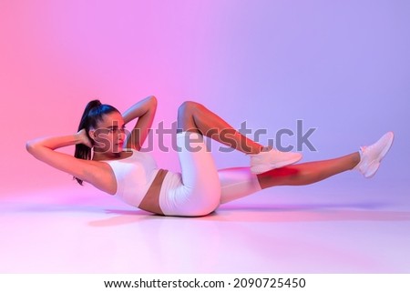 Fitness Workout. Sporty Woman Doing Bicycle Crunch Abs Exercise Lying On Floor Over Pink And Blue Neon Studio Background. Determined Lady Wearing White Fitwear Training Flexing Abdominal Muscles Сток-фото © 
