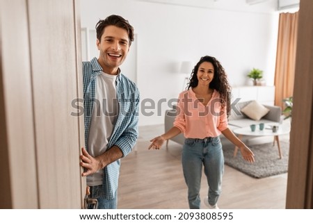 Portrait of cheerful couple welcoming inviting guests to enter home, happy young guy and lady standing in doorway of modern flat, looking out together, waiting for visitor friends to come in Foto stock © 