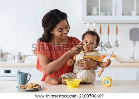 Baby Weaning. Caring Black Mother Feeding Little Toddler Son From Spoon In Kitchen, Loving African American Mommy Giving Porridge Or Mash Fruit Puree To Cute Little Child At Home, Closeup Shot Photo stock © 