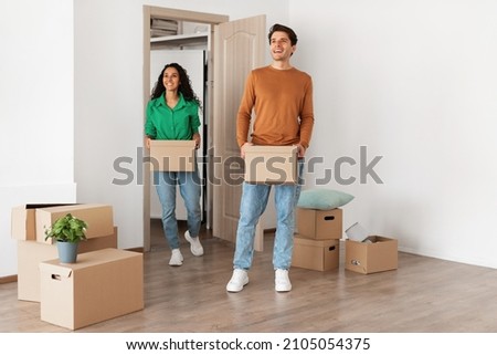 Family Housing Concept. Happy couple walking in new apartment and looking around, smiling young guy and lady holding cardboard boxes standing in modern home. Real estate dwelling, mortgage Foto stock © 