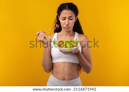 Dieting Concept. Portrait Of Unhappy Lady Holding Bowl With Vegetable Salad And Fork Looking At Meal Standing Isolated On Yellow Orange Studio Background. Loss Of Taste And Smell, Lack Of Appetite Stock foto © 