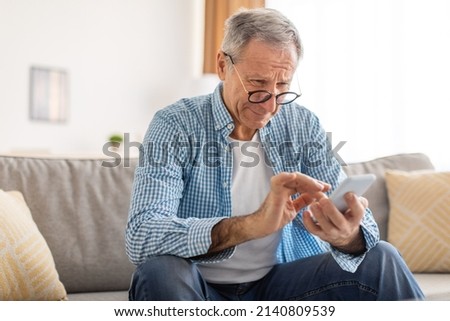 Poor Eyesight In Older Age, Macular Degeneration Concept. Confused Mature Male In Eyeglasses Squinting Eyes Reading Message On Cell Phone Having Ophtalmic Issue Problems With Vision Sitting On Sofa Stok fotoğraf © 