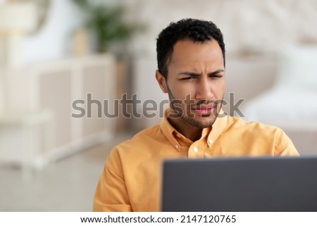 Closeup portrait of confused Arabic guy sitting on couch using laptop, looking at pc screen and squinting. Worried man reading bad negative news, having problems and poor eyesight Foto d'archivio © 